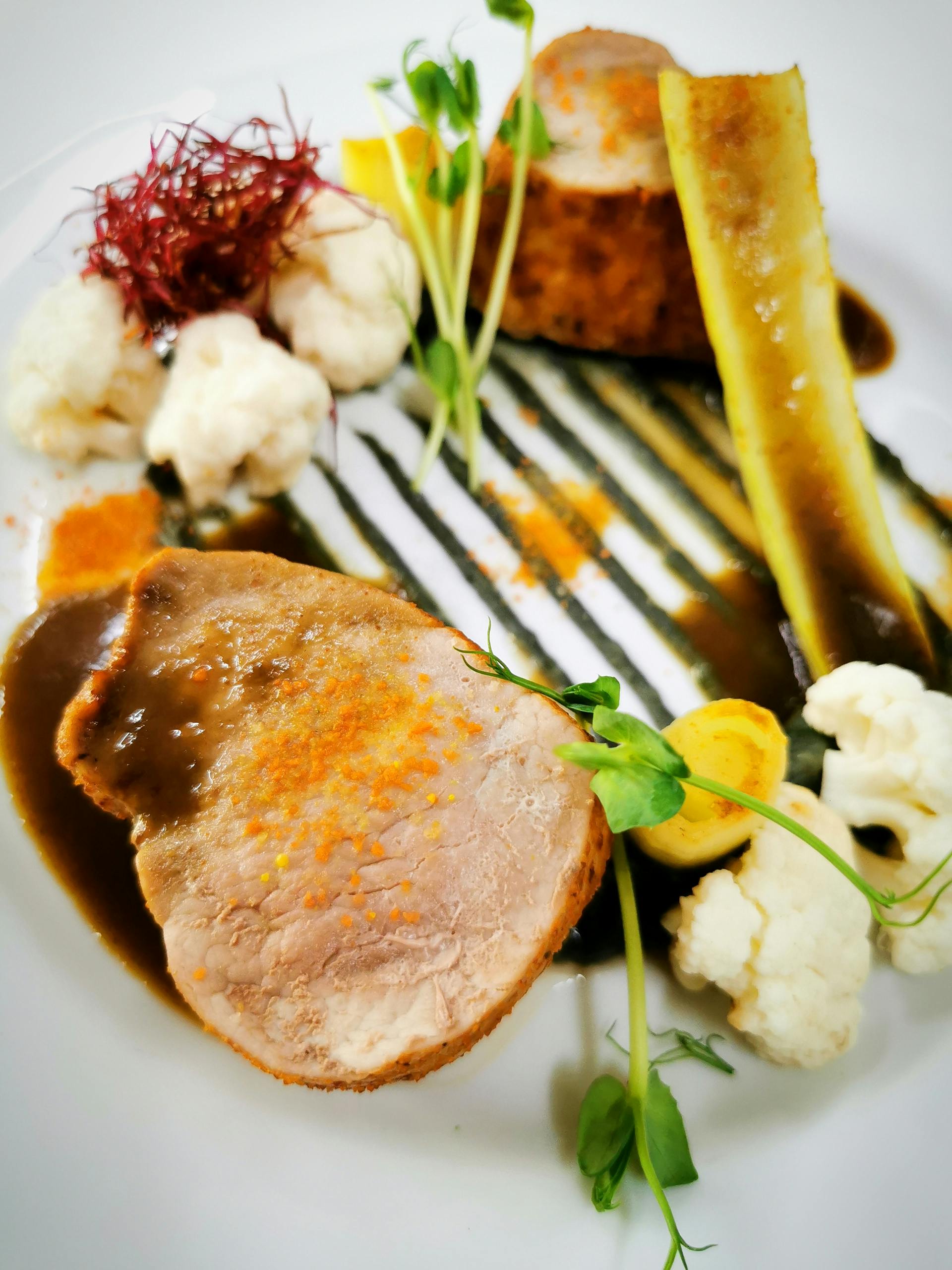 A gourmet dish featuring pork, cauliflower, and artful garnishes on a white plate.