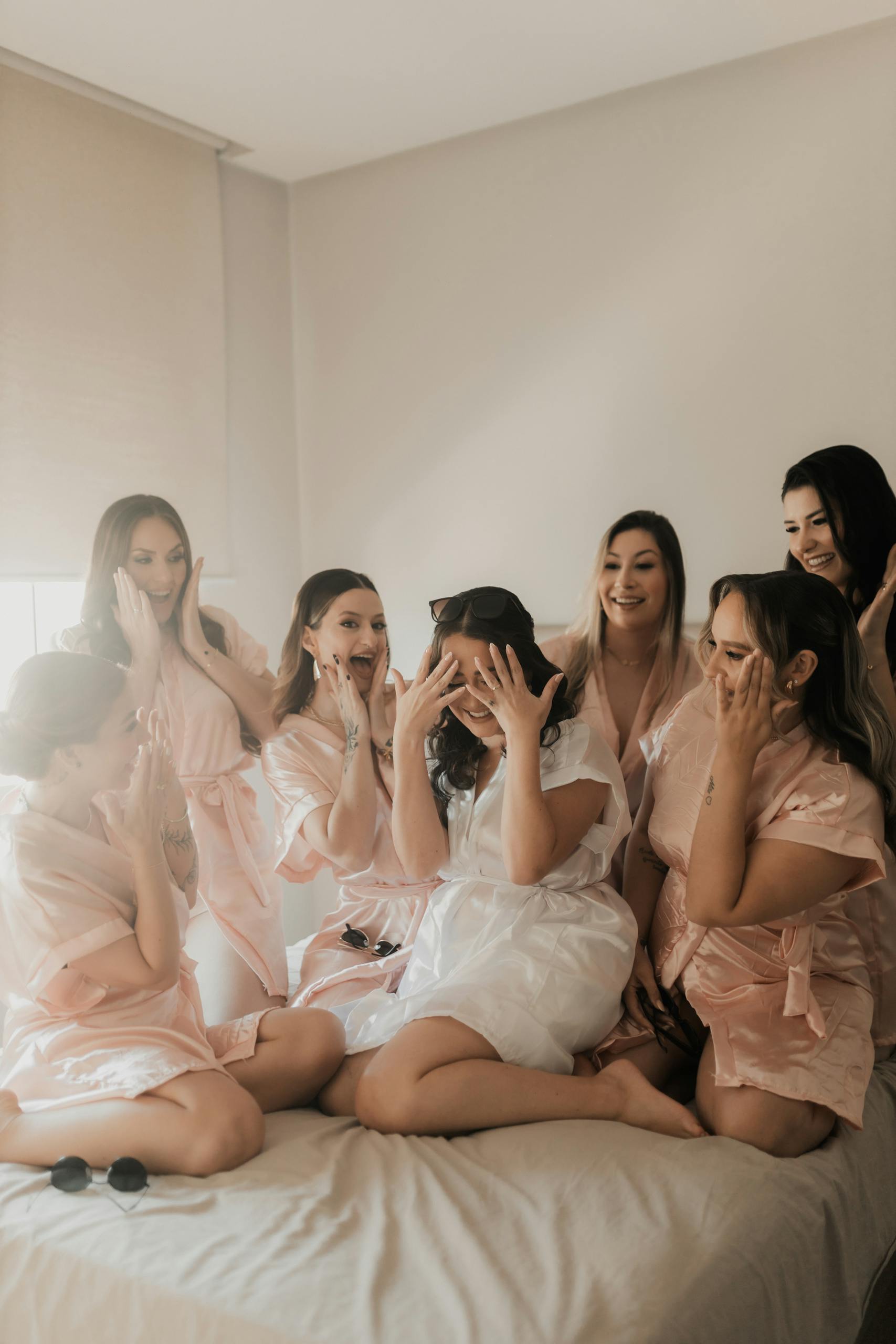 Joyful bridal party in pink and white robes celebrating together indoors. Perfect for wedding and lifestyle themes.