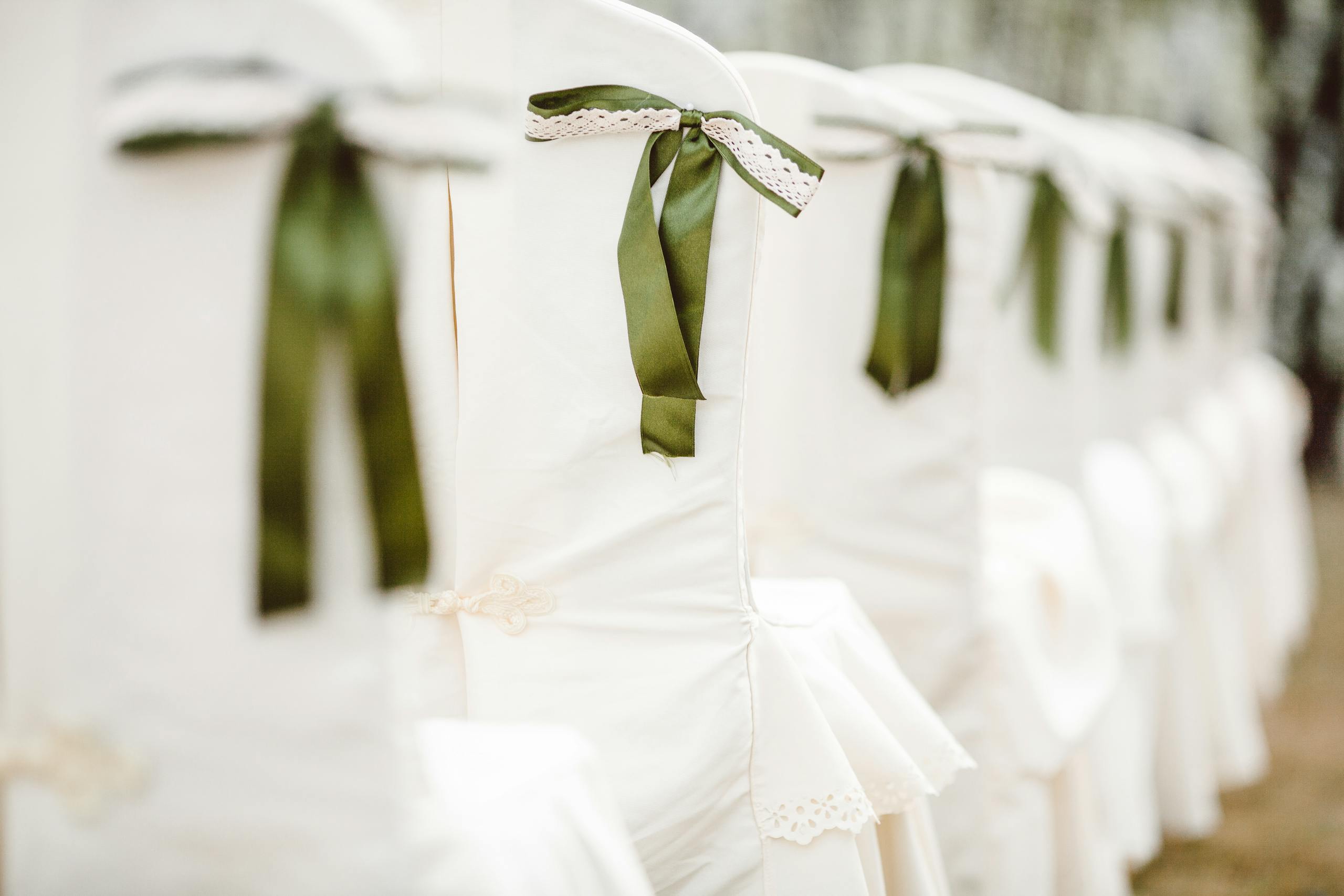 White chairs adorned with green ribbon bows, perfect for a wedding or elegant event setup.